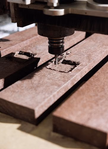 Máquina de CNC a gravar baixo relevo em perfil de plástico reciclado castanho.